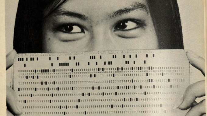 Scanned image of the magazine ad for China Data Systems, illustrated by a photo of a woman holding a computer punchcard in front of her mouth and nose, so that only her eyes and hairline are visible.